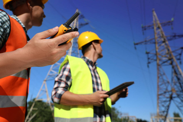Professional electricians near high voltage towers, focus on hand with portable radio station - Fotó, kép