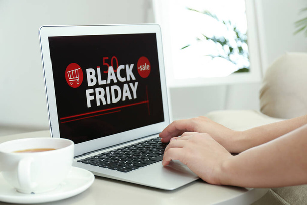 Woman using laptop with Black Friday announcement on screen at table, closeup - 写真・画像