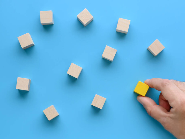 Hand déplace un cube en bois vers le groupe de cubes sur fond bleu. - Photo, image