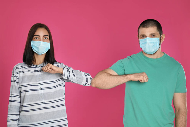Man and woman bumping elbows to say hello on pink background. Keeping social distance during coronavirus pandemic - Photo, image