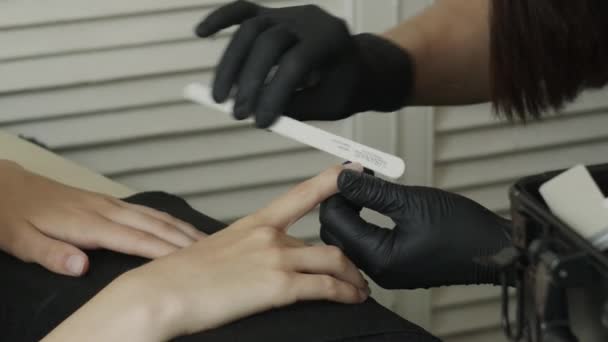 Nail artist is doing manicure with a nail file. She is wearing black gloves. - Footage, Video