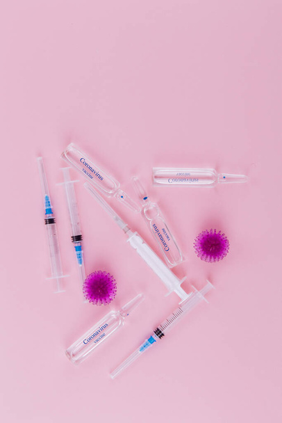 Abstract model of coronavirus infection of the strain Coronavirus. Red virus, syringe and ampoules with medicine on a pink background. On ampoules the blue inscription Coronavirus vaccine. Copy space. - Photo, Image