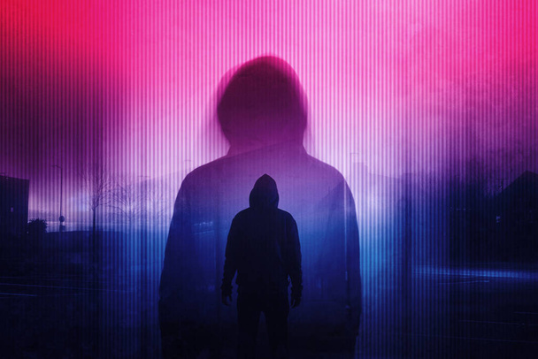 A double exposure of a Silhouette of a mysterious hooded figure without a face. Standing in a city at night. With a glitch, neon edit - Fotoğraf, Görsel