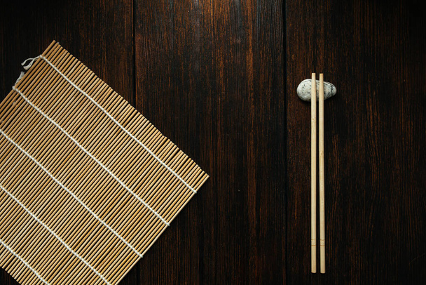 mat for rolls and chopsticks for chinese asian food on dark wooden background top view. Asian cutlery. - Zdjęcie, obraz