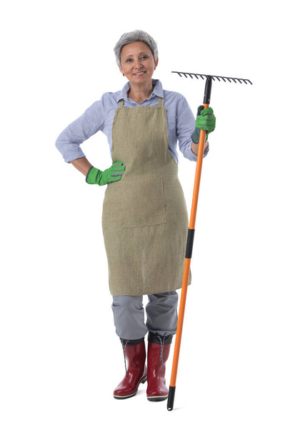 Gardening. Mature woman gardener worker with rake isolated on white background, full length portrait - Фото, изображение