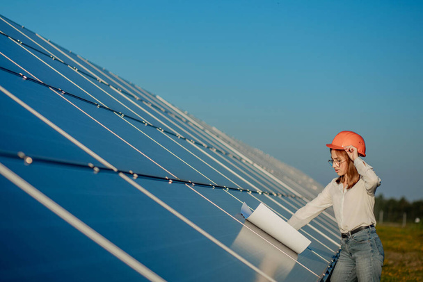 Handsome Architect Woman Examining a Draft Map or Blueprint Project Plan, Worker Activity Looking Out in Photovoltaic Cell Farm or Solar Panels Field. - Photo, Image