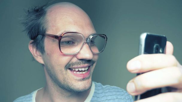 funny balding man in glasses uses a smartphone and smiles - Фото, зображення