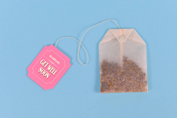 Tea bag with made up cute pink label with text 'Get well soon' on pastel blue background - 写真・画像
