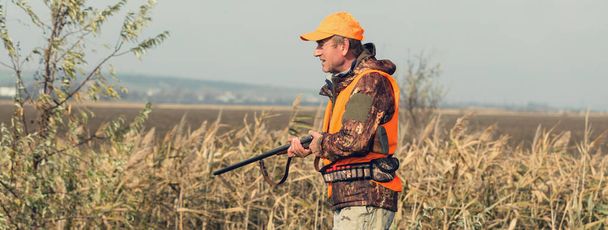 Homme chasseur dans un champ rural avec fusil de chasse et sac à dos pendant la saison de chasse - Photo, image
