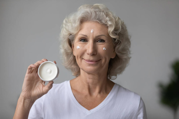 Head shot portrait satisfied mature woman holding moisturizing cream jar - 写真・画像