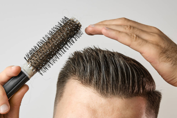 Людина використовує круглу щітку для укладання волосся. Догляд за волоссям вдома після перукарні. Розчісування короткого коричневого волосся на білому тлі
 - Фото, зображення