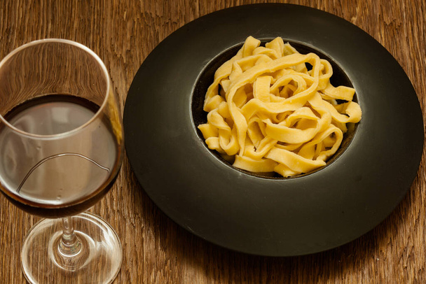 Итальянская паста на черной тарелке с бокалом вина - Фото, изображение