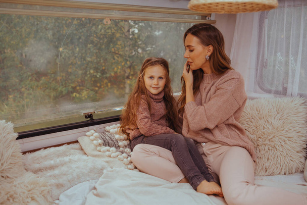 Glückliche Familie - Mutter und kleine Tochter entspannen sich beim Umarmen und haben Spaß in der Natur in einem weißen skandinavischen rustikalen Wohnmobil-Interieur. Inländisches Tourismuskonzept  - Foto, Bild