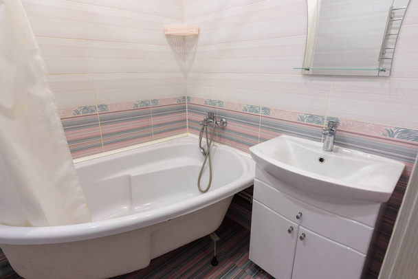 Interieur van een gezellige gewone badkamer met wastafel, ligbad en spiegel - Foto, afbeelding