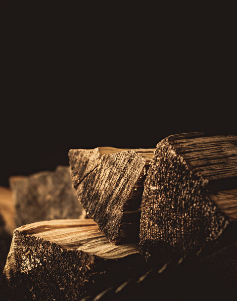 Chipped firewood lie near the fireplace on a dark background - Foto, afbeelding