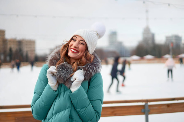 Beautiful lovely middle-aged girl curly hair warm winter jackets white knitted hat glove stands ice rink background Town Square Christmas mood lifestyle Happy holiday woman  snowy day Winter leisure  - Fotó, kép