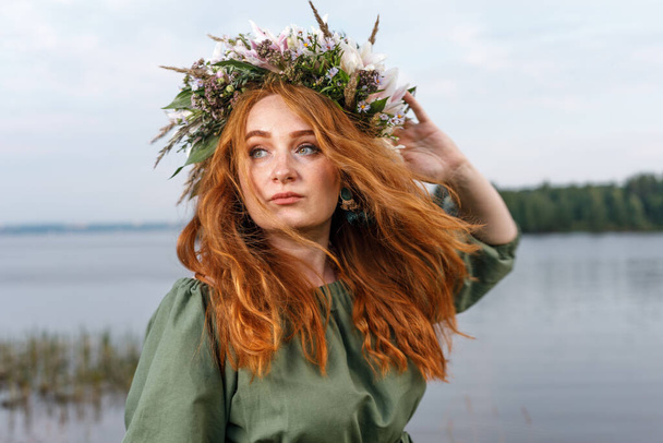 Slavic beauty with a flower wreath on her head in the lap of nature. Ancient pagan origin celebration concept. Summer solstice day. Mid summer. - Foto, afbeelding