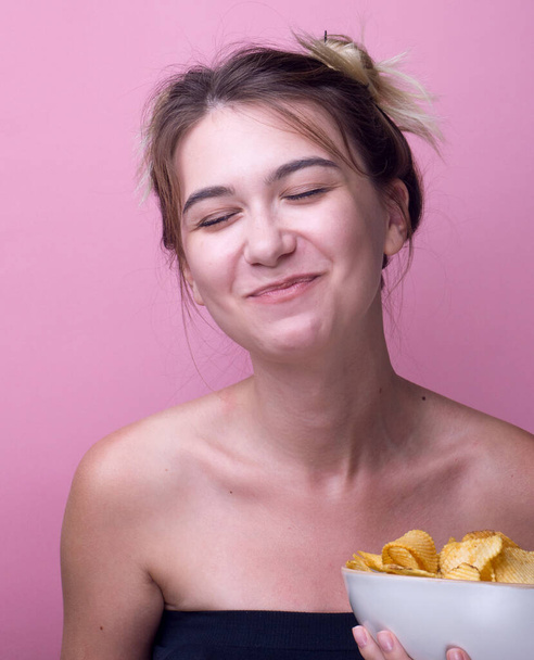 Hladové legrační Žena jíst bramborové lupínky na barevném růžovém pozadí. Atraktivní, šťastná dívka jí smažené brambory. Detailní portrét ateliéru. Izolovaný. nezdravá svačina, panorama - Fotografie, Obrázek