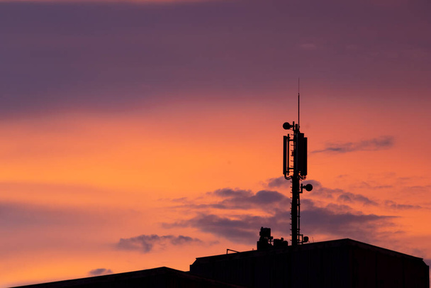 Matkaviestinnän torni antenni siluetti kaunis auringonlasku oranssi ja sininen taivas näyttää modernin teknologian infrastruktuuri internet ja matkapuhelimet kaupunkimaisemassa streaming palvelu - Valokuva, kuva