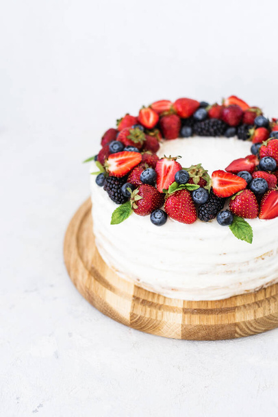 Rustic cake with fresh berries. Delicious fresh cake on a white background. Strawberry cake with blueberries and mint. Homemade blueberry vanilla cream cake - Photo, Image