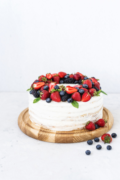 Rustikaler Kuchen mit frischen Beeren. Köstlicher frischer Kuchen auf weißem Hintergrund. Erdbeerkuchen mit Blaubeeren und Minze. Hausgemachte Blaubeeren-Vanille-Sahnetorte - Foto, Bild