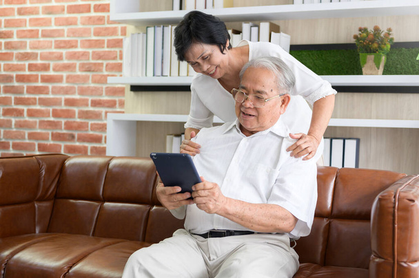 A happy senior Asian couple is using tablet and talking with family on webcam at home, retirement concept. - Fotografie, Obrázek