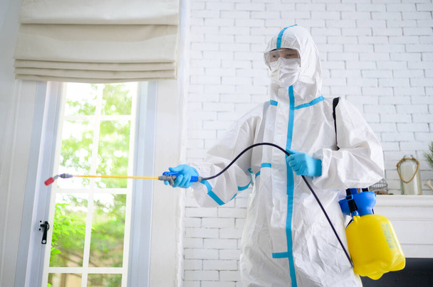 Медицинский персонал в костюме СИЗ использует дезинфицирующий спрей в гостиной, защиту Covid-19, концепцию дезинфекции . - Фото, изображение
