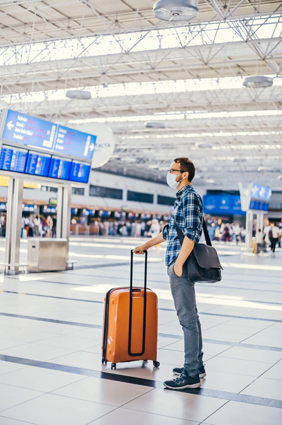 Airport european nerd man in glasses and plaid shirt with luggage tourist boarding plane taking a flight  wearing face mask. Coronavirus flu virus travel  - Photo, Image