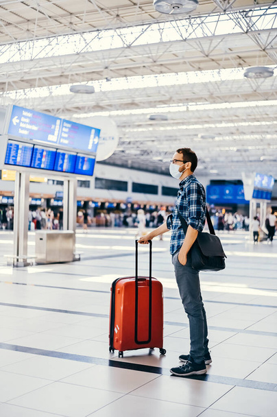 Airport european nerd man in glasses and plaid shirt with luggage tourist boarding plane taking a flight  wearing face mask. Coronavirus flu virus travel  - Photo, Image