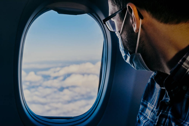 Hombre nerd europeo del aeropuerto en gafas y camisa a cuadros con equipaje avión de abordaje turístico tomando un vuelo con máscara facial. Viaje del virus de la gripe por el coronavirus  - Foto, imagen