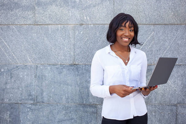 Estudante afro-americano com rosto feliz usando computador portátil para educação remotamente ao ar livre., posando em fundo cinza. Espaço de cópia vazio. - Foto, Imagem