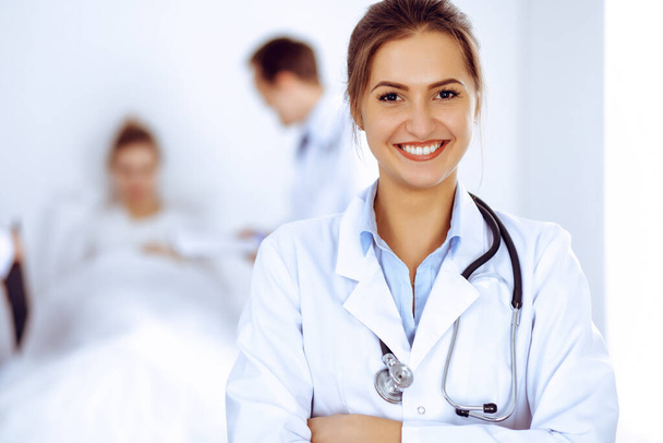 Female doctor smiling on the background with patient in the bed and two doctors - Фото, изображение