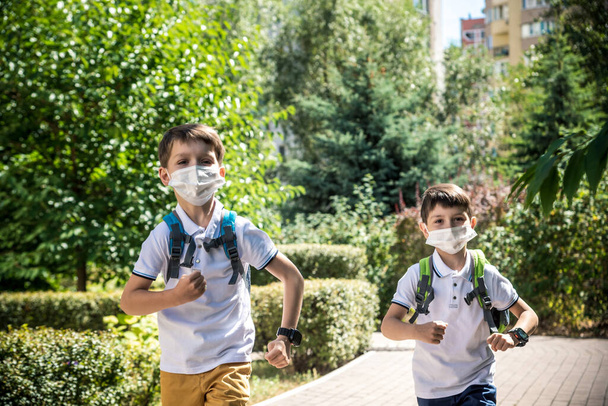 Gelukkige schoolkinderen met gezichtsmaskers lopen weg van de vreugde om terug te keren naar school tijdens de Covid-19 quarantaine. - Foto, afbeelding