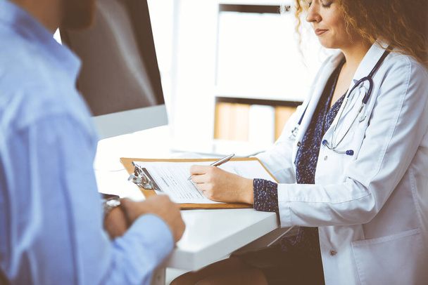Female doctor and male patient discussing current health examination while sitting in clinic, close-up. Medicine concept - Foto, imagen