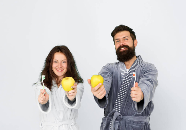Brush teeth concept. Oral hygiene. Couple in bathrobes hold toothbrushes and apples. Man girl care hygiene. First rule of personal hygiene. Couple in love cleaning teeth every morning. Healthy smile - Fotó, kép