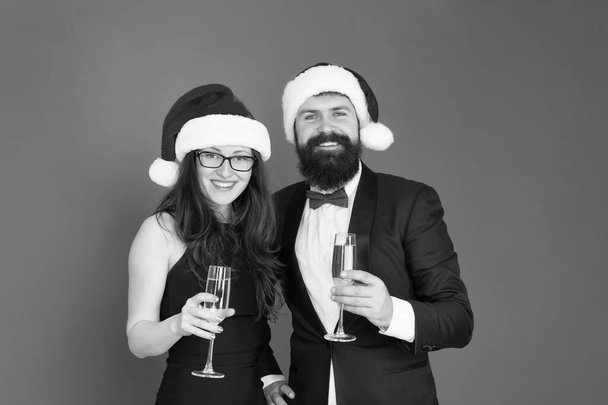 Sincere greetings. Merry christmas. Office party. Couple at corporate party. Happy new year. Bearded businessman in tuxedo and girl elegant dress drinking sparkling wine red background. Winter party - Foto, afbeelding
