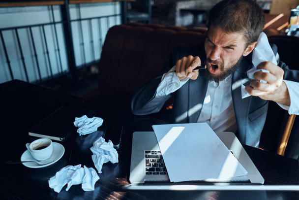 Bir kafede oturan bir iş adamı laptopunu buruşmuş kağıt yöneticiliği yaşam tarzı duyguları ile doldurur. - Fotoğraf, Görsel