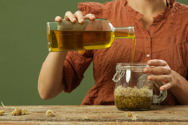 Žena vyrábějící bylinný olej se žlutými květy. Proces macerace pro přírodní organickou kosmetiku. - Fotografie, Obrázek