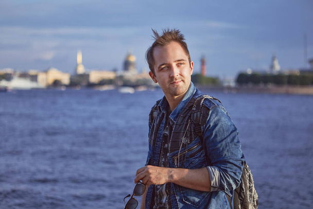 Portrait of young man on the background of the river in european city. Caucasian male tourist 27 years old is travelling in Europe. - Фото, изображение