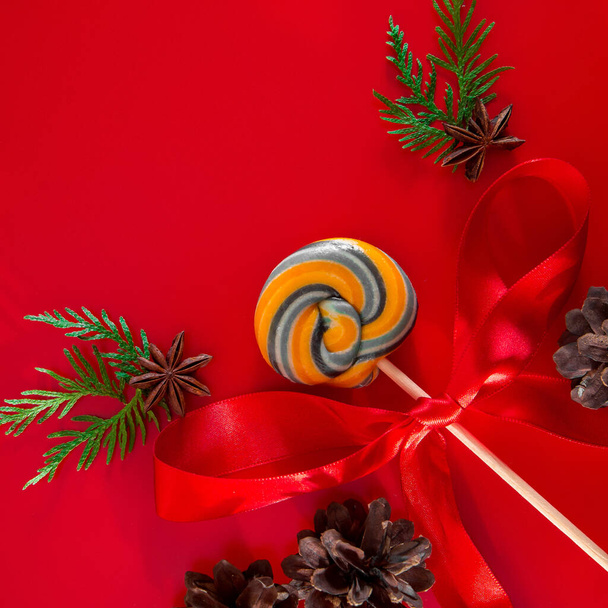Süßer Lutscher und Tannenzweige mit Zapfen. Weihnachtskomposition auf rotem Hintergrund. Platz für Text - Foto, Bild