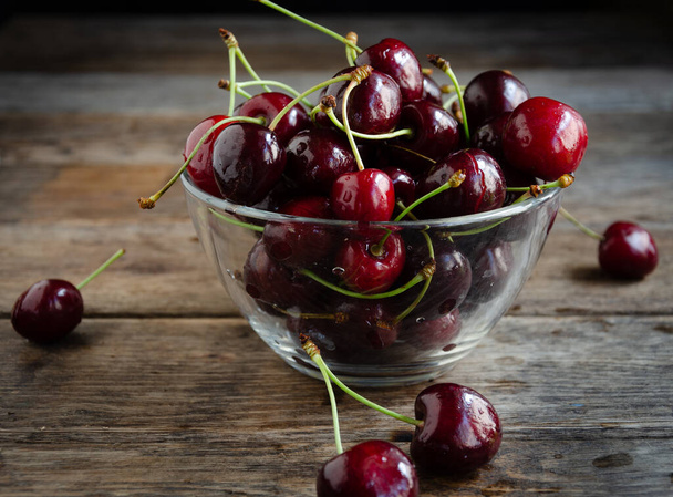 Ripe red cherries in glassware on a wooden background. - Foto, Imagem