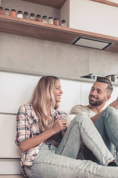 young couple drinking coffee sitting on the kitchen floor - Photo, Image