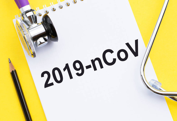 2019-nCov geschreven op notebook met stethoscoop op gele achtergrond. Concept voor wereldwijde dekking van de ernst van het Covid-19 of 2019-ncov-virus. - Foto, afbeelding
