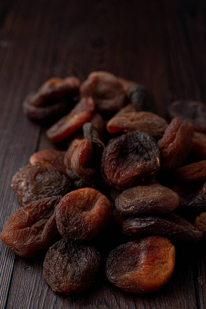 Pile of dark sun dried apricots on dark wooden table, close up - Photo, Image