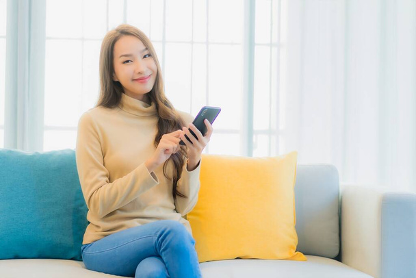 Portrait beautiful young asian woman with smart mobile phone on sofa in living room interior - Фото, зображення