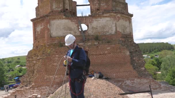 construction engineer evaluates the volume of work at height. An industrial climber in protective clothing is tied with a safety rope on the emergency roof of a building. high-altitude worker - Footage, Video