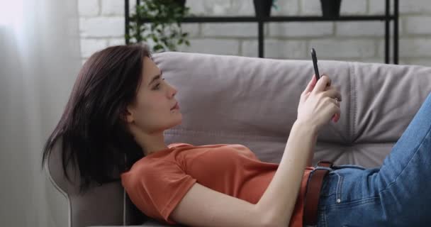 Relaxed girl lying on couch with smart phone - Video