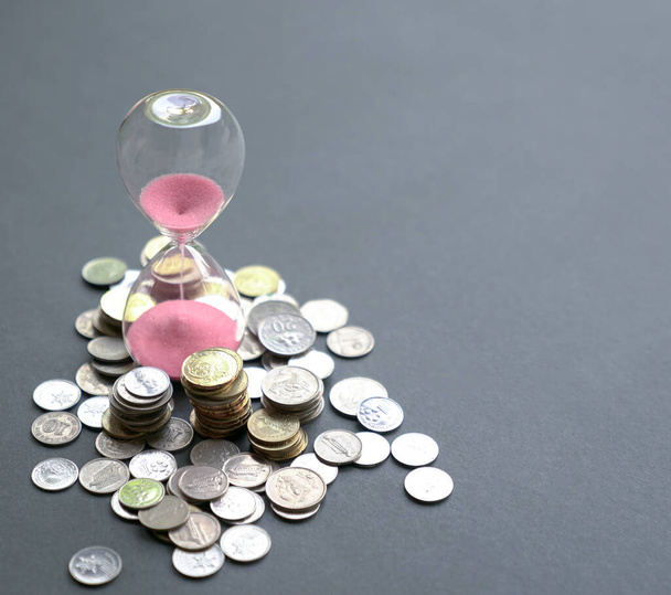 Hourglass with sand flowing and coins on table. Time is money concept. - Foto, Imagem