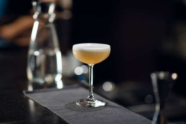 Een glas met een felgele alcoholische cocktail op de bar en de handen van een barman in een nachtclub. - Foto, afbeelding