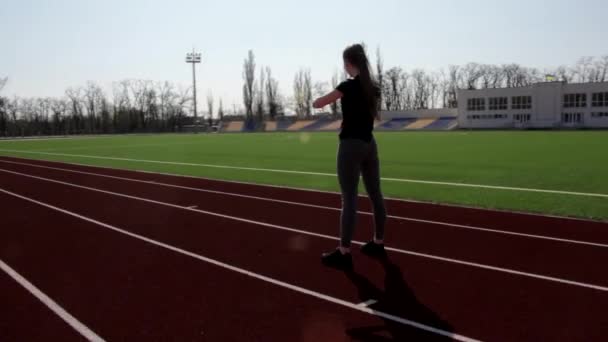 Подходит молодая привлекательная активная спортсменка делает приседания разминать мышцы на открытом воздухе тренировки снаружи большой стадион - Кадры, видео